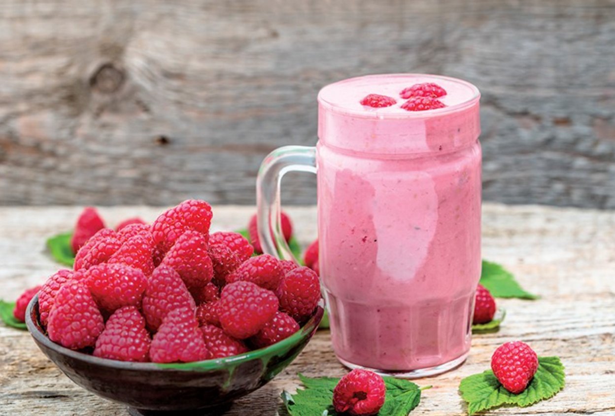 himbeer-shake in einem glas auf einem holztisch mit einer schale frischer himbeeren